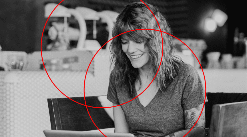 Immagine in bianco e nero di una donna che sorride al computer, con la grafica di due cerchi rossi.
