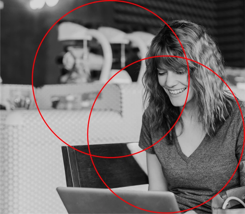 Immagine in bianco e nero di una donna che sorride al computer e due cerchi rossi in grafica.