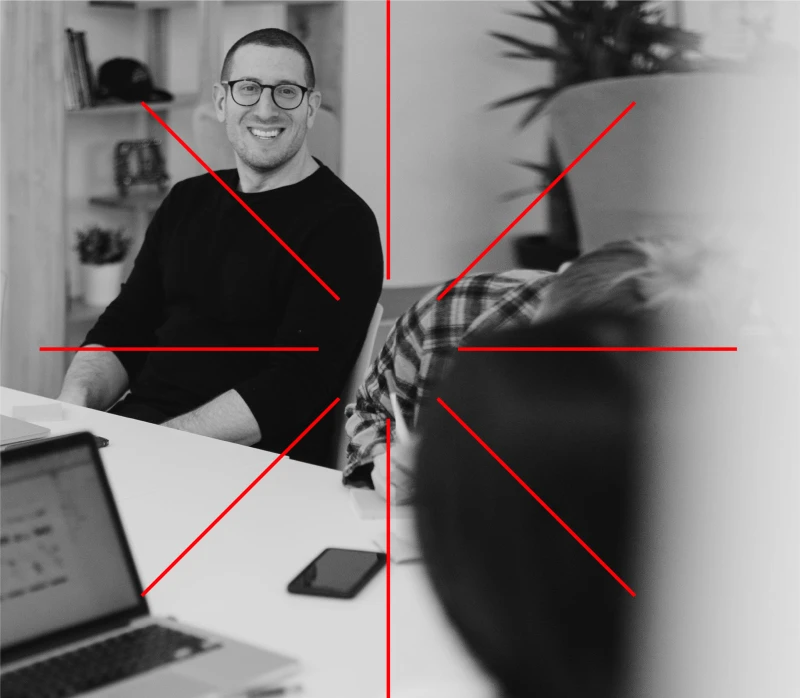 Immagine in bianco e nero di un uomo sorridente al computer, con una grafica dalle linee rosse che creano una stella stilizzata.