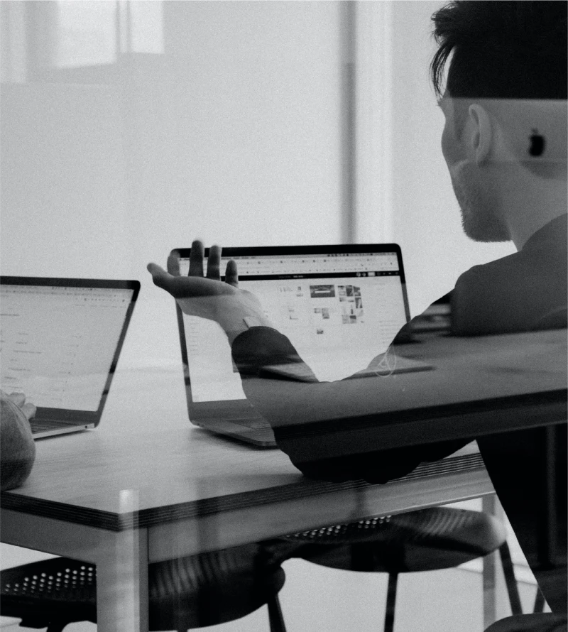 Immagine in bianco e nero di un uomo al computer, con un altro schermo di computer sul lato sinistro.